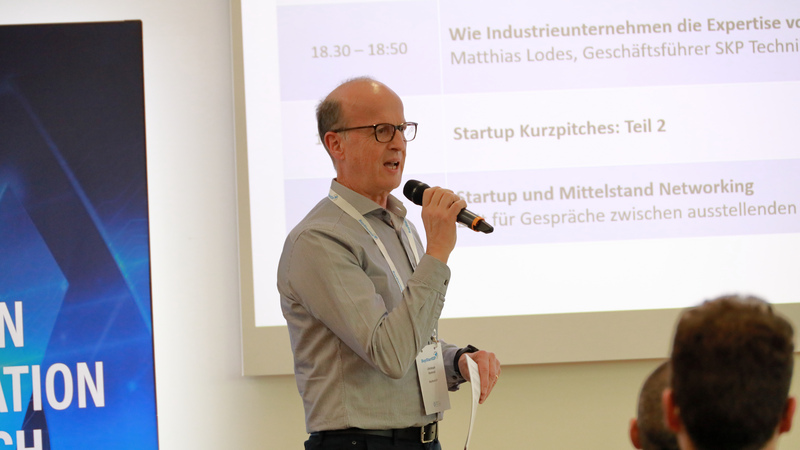 Christoph Rommel von BayStartUP spricht Begrüßungsworte in ein Mikrophon und leitet in die Veranstaltung ein.